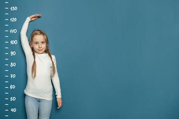 Kid girl measures the growth on blue background. Education and grow up concept