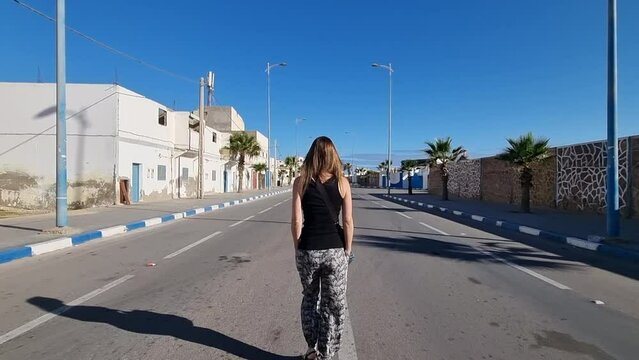 Girl with long hair walks in the middle of a deserted street in Casa del mar, Tarfaya,, Marroco. 4K videos. Beautiful girl walking with her back to the camera.