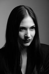 Fashion concept. Beautiful woman with dark hair and lipstick in dark lighting black and white studio portrait. Model looking aside the camera and wearing black classic suit. Part of face is in shadow