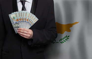Cypriot business man showing 100 US dollar bills against flag of Republic of Cyprus background