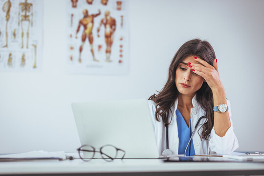 Woman doctor on stress sitting at desk with hand on head in ambulance.  Worried mature doctor having some problems while working on laptop in the office.