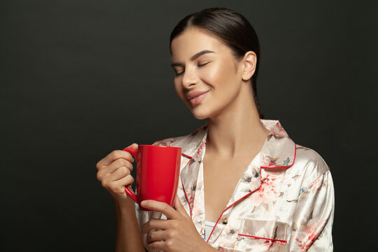 Young brunette woman with red mug enjoying coffee against black background