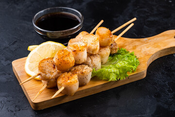 Grilled sea scallops without shells lie on a wooden board, dark table. Sea scallop appetizer.