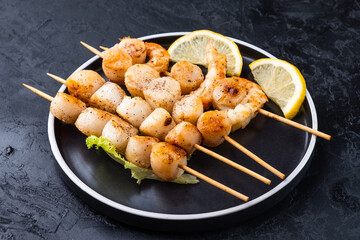 Scallop and shrimp seafood skewers served on a dark plate, dark background.