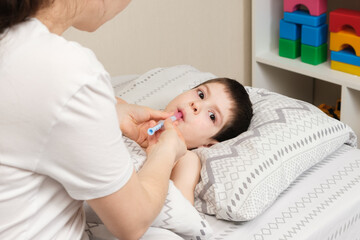 Obraz na płótnie Canvas A mother or doctor gives a 4-year-old child a medicine for fever or cough. Treatment of children from bronchitis, pneumonia, antibiotics in pediatrics.