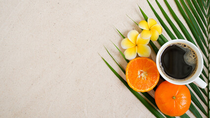 cup of coffee with flowers and fruits on sand.