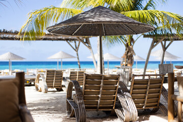 Wooden chairs and sun loungers with sun umbrellas on a tropical beach. Beach club.