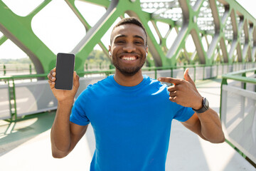 Fototapeta premium Portrait of a positive, guy holding a smartphone with a black screen in his hand, pointing his finger at the product