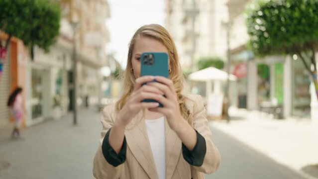 Young blonde woman smiling confident making photo by the smartphone at street