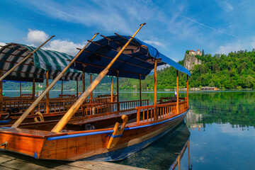 Naklejka na ściany i meble Traditional Pletna boat on the Bled lake. A boat that transports tourists to the island where the church Assumption of Maria .In the background is the famous old castle on the cliff. Bled, Slovenia