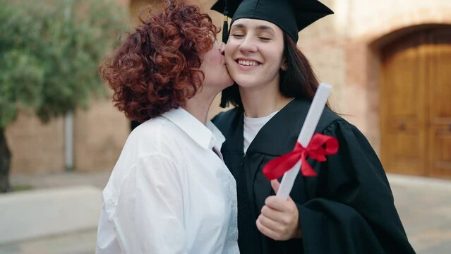 Two women mother and daughter hugging each other holding diploma at campus university