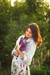 Calm portrait of a feminine dreamy girl with closed eyes hugging a bouquet of purple lupins