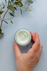 Skin care product. Female hand holding a face cream jar on pastel blue purple background,...
