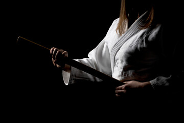 A girl in black hakama standing in fighting pose with wooden sword bokken over dark background. Shallow depth of field. SDF. 