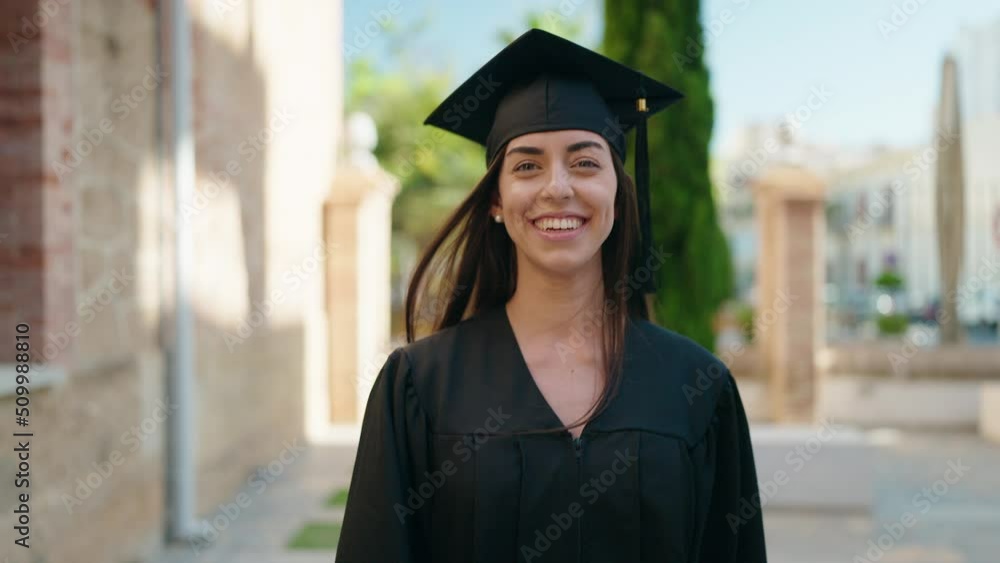 Sticker Young hispanic woman wearing graduated uniform walking at university