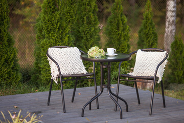 Fototapeta na wymiar Real photo of a modern garden chair withmacrame pillow standing on a wooden deck in the garden of a weekend retreat