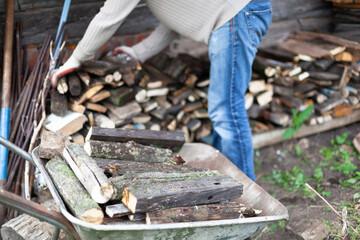 A man puts firewood from a cart into a firewood storage