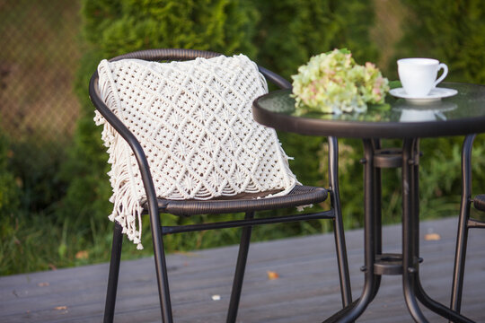 Real photo of a modern garden chair withmacrame pillow standing on a wooden deck in the garden of a weekend retreat