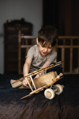 a five-year-old boy is playing at home on a bed with a large wooden airplane. The child spends time with toys