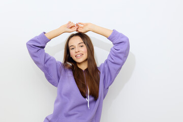 Fototapeta na wymiar a gentle beautiful woman stands on a white background in a purple tracksuit raises her arms above her head smiling sweetly