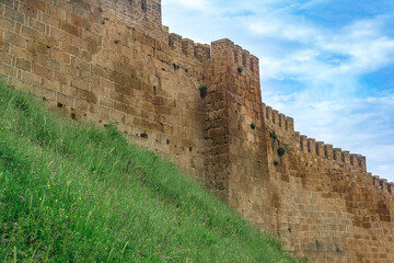 Fototapeta premium wall of a medieval fortress above a rampart overgrown with grass against the sky, Naryn-Kala citadel in Derbent