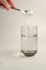 Woman pours collagen powder or protein in a glass of water on a beige background. A healthy and...