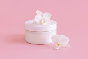 Fototapeta na wymiar White cream jar near white orchid flowers on light pink close up. Mockup. Skincare product