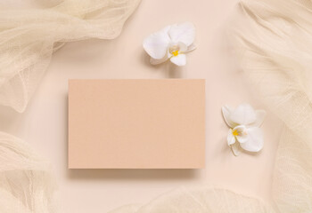 Blank card near white orchid flowers and tulle on light yellow top view, mockup