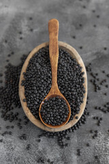Bowl of dry black lentils beans with a spoon on grey table close up, protein source for vegetarian diet