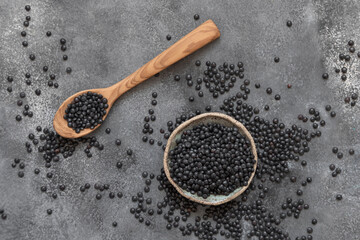 Bowl and spoon of dry black lentils beans on grey table top view, protein source for vegetarian diet
