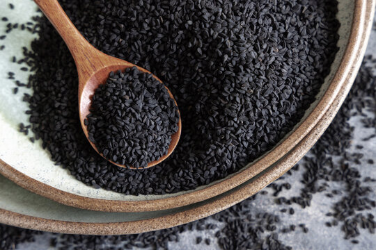 Plate of Indian spice Black cumin (nigella sativa or kalonji) seeds close up with a wooden spoon