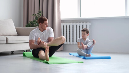 Fototapeta na wymiar Father and Son do Spotting. Sport at Home. Warm Up in Quarter. Lying on Gymnastic Mat. Doing Sports. Man and Boy Train at Home.
