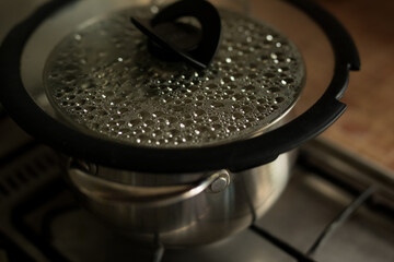 a pot of water is boiling on a stove. condensate bubbles under the glass lid