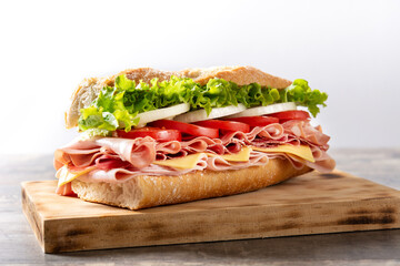 Submarine sandwich with ham, cheese, lettuce, tomatoes,onion, mortadella and sausage on wooden table	