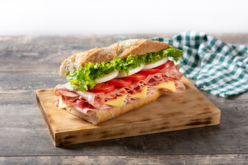 Submarine sandwich with ham, cheese, lettuce, tomatoes,onion, mortadella and sausage on wooden table	 - obrazy, fototapety, plakaty