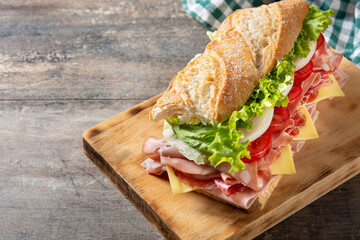 Submarine sandwich with ham, cheese, lettuce, tomatoes,onion, mortadella and sausage on wooden table	