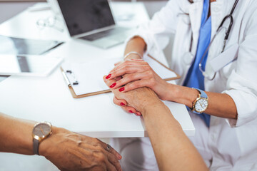 Female doctor holding hands of female patient at meeting as women health medical care concept...