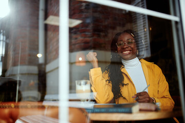 A clever african girl sits in a coffee shop and writes homework in her textbook.