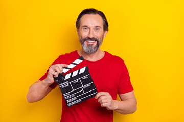 Photo of cheerful positive guy pensioner dressed red t-shirt holding clapperboard isolated yellow...