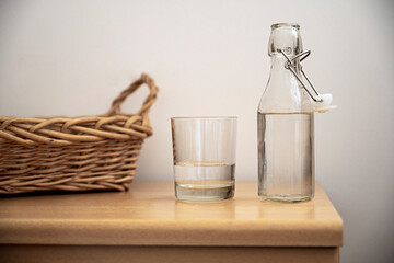 Glass bottle and a drinking glass with water on woodent table, indoor. Drinking water, healthy lifestyle.