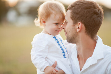 Beautiful young dad and his little blue-eyed curly 1 year old daughter in light natural clothes are...