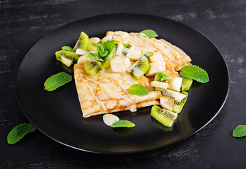 Crepes, thin pancakes or blini with kiwi and banana in black plate. Pancake week. Shrovetide.