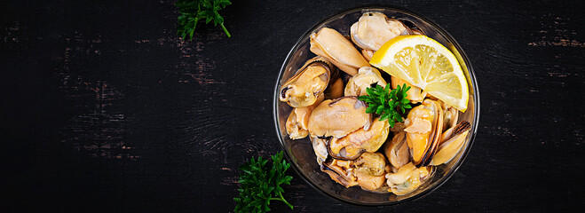 Delicious mussel meat with lemon and fresh parsley on a dark background. Top view, banner