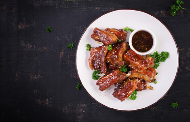 Delicious barbecued spare ribs on plate on dark background. Tasty bbq meat. Top view, flat lay