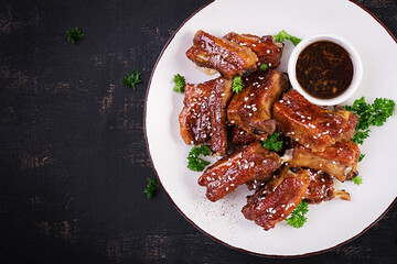 Delicious barbecued spare ribs on plate on dark background. Tasty bbq meat. Top view, flat lay