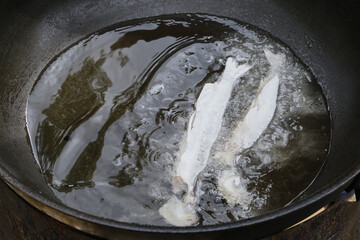 Two small fish fry on a pan in oil. Shallow depth of field
