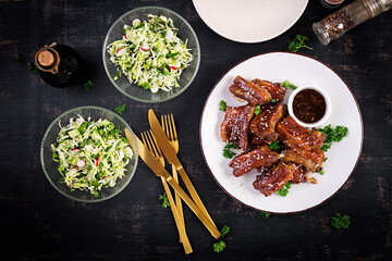 Delicious barbecued spare ribs on plate on dark background. Tasty bbq meat. Top view, flat lay