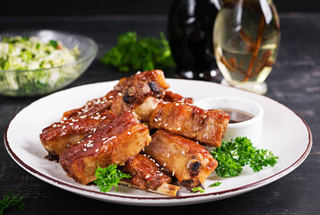 Delicious barbecued spare ribs on plate on dark background. Tasty bbq meat.