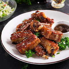 Delicious barbecued spare ribs on plate on dark background. Tasty bbq meat.