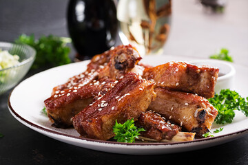 Delicious barbecued spare ribs on plate on dark background. Tasty bbq meat.